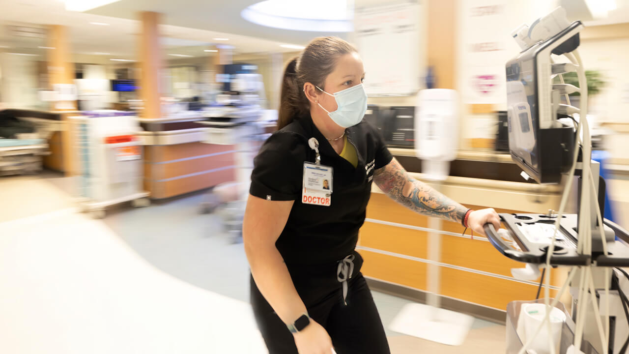 Nurse pushing a cart of medical technology.