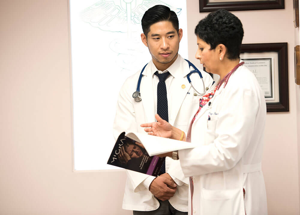 A medical student stands and listens to his faculty mentor as she shows him a booklet in her practice