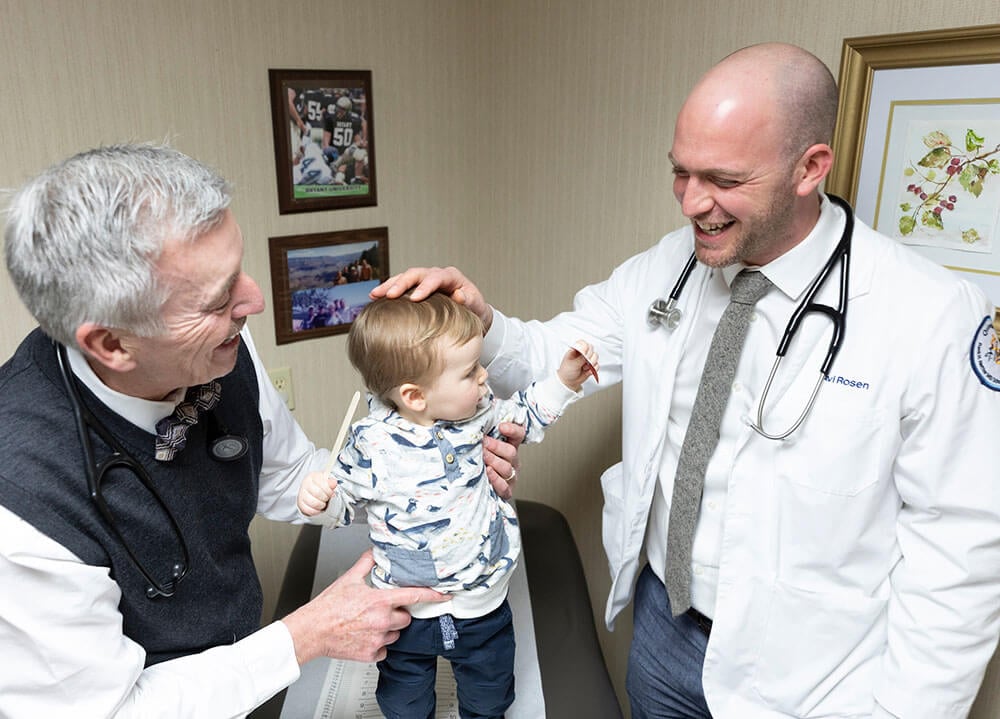 A Netter student wearing a medical coat and stethoscope works with an 11-month-old patient