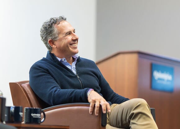 Quinnipiac Board of Trustees Chairman Chuck Saia smiles while sitting in a chair.