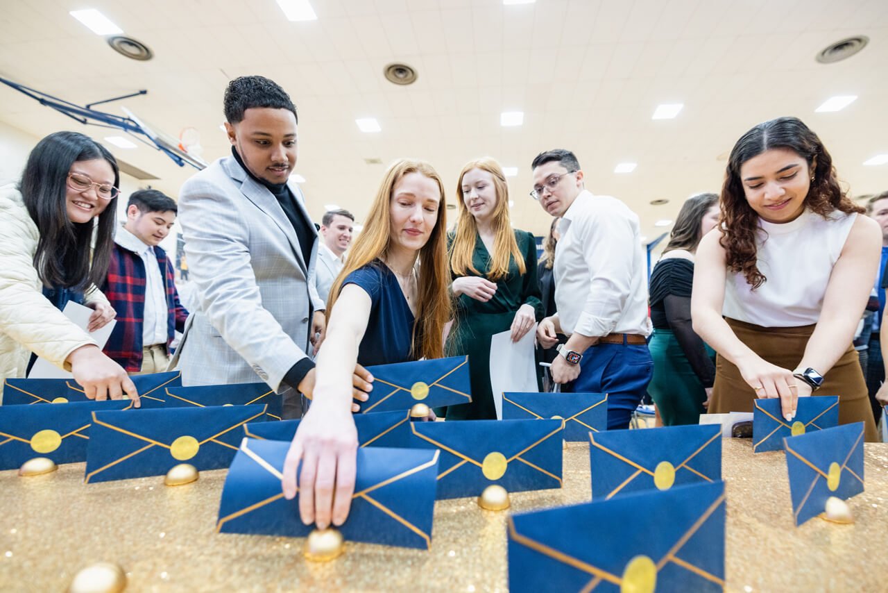 Half a dozen medical students pick up their navy blue and gold match day envelopes from a table