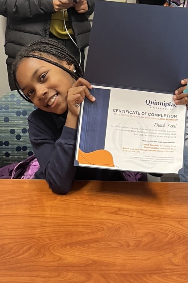 A participating student, smiling, while holding a certificate of completion for the program.