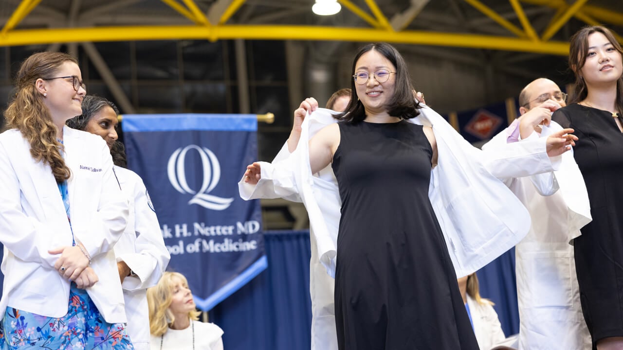 Faculty put white coats onto three new medical students as they smile