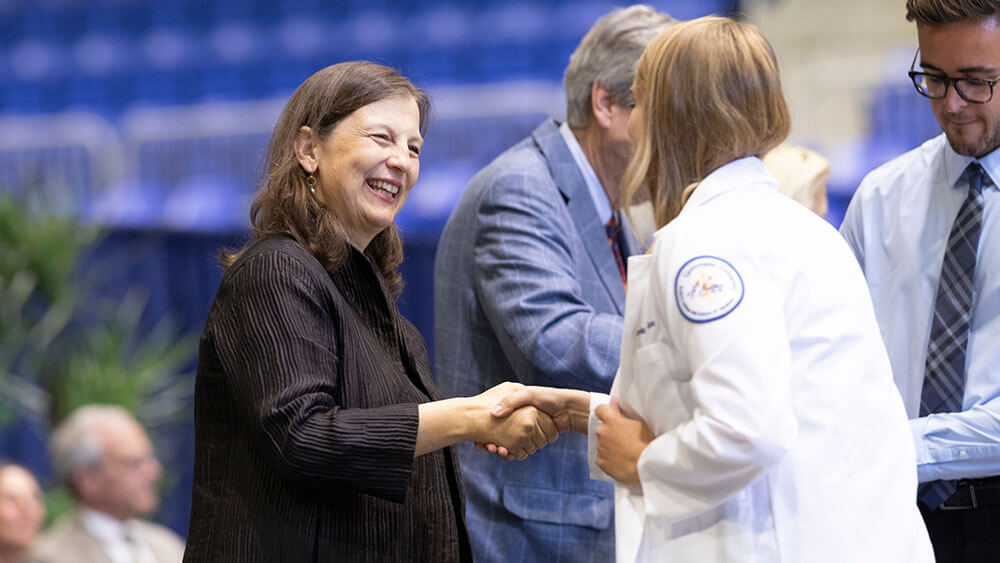 A Netter administrator smiles and shakes the hand of a student receiving her white coat