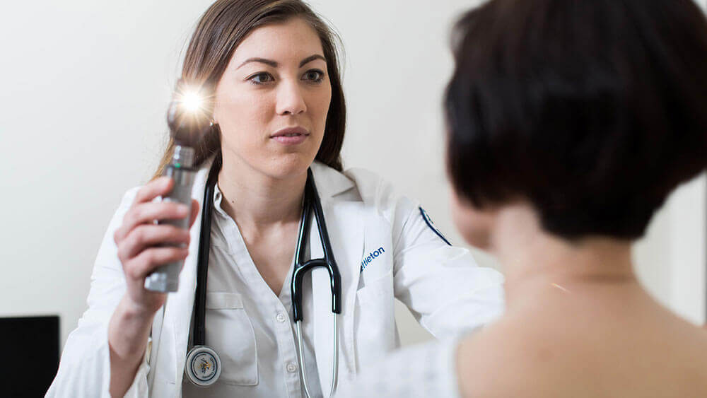 A medical student uses a light to examine the eyes of her patient