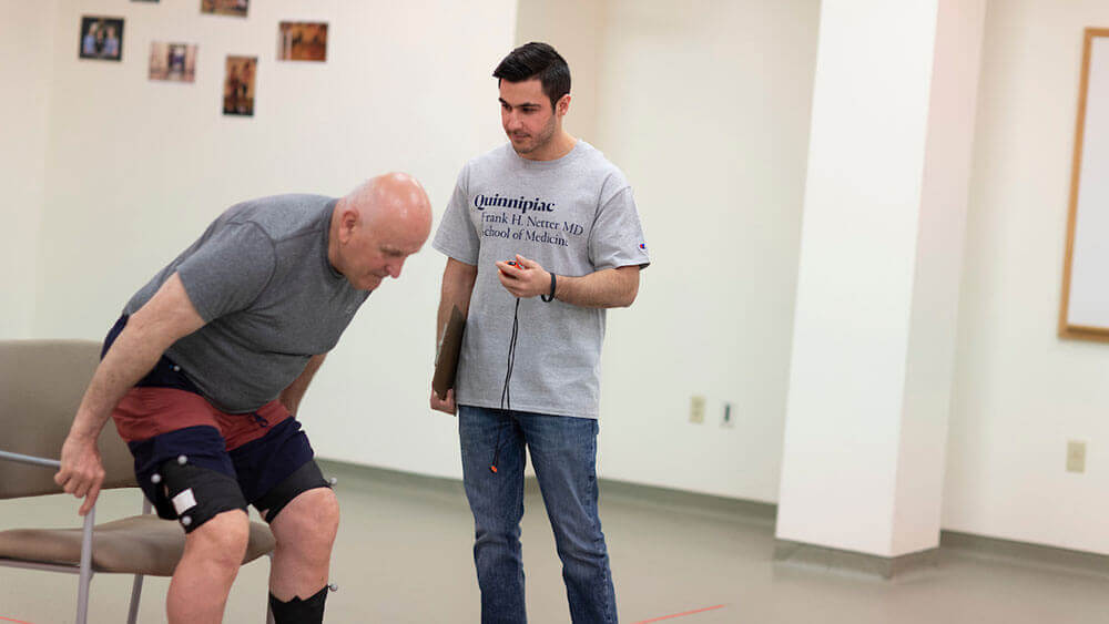 A medical student with a stopwatch assists a physical therapy patient in the motion analysis lab