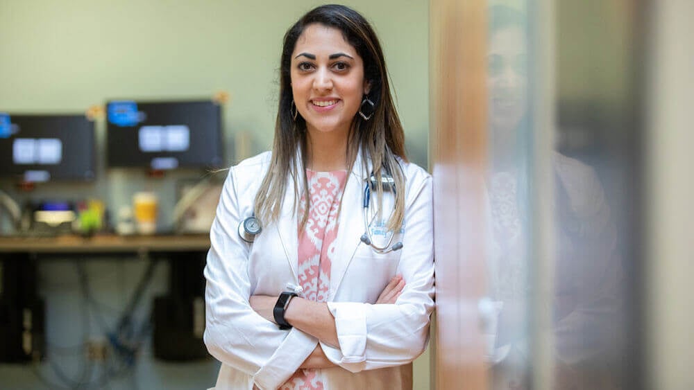 Med student Rana Alhaldi poses in the doorway of her office wearing her white coat and stethoscope
